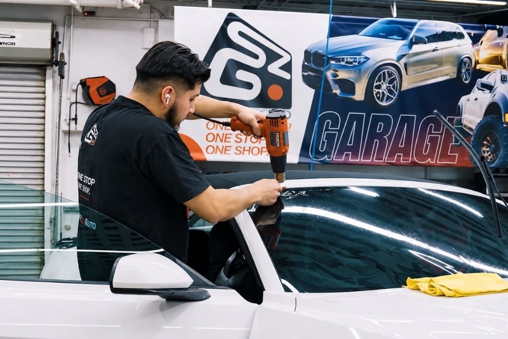 Soundz Good Garage technician heat-shrinking window tint film on a car windshield.