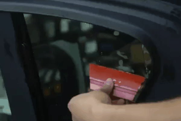Technician using a squeegee to apply window tint film to a vehicle side window.