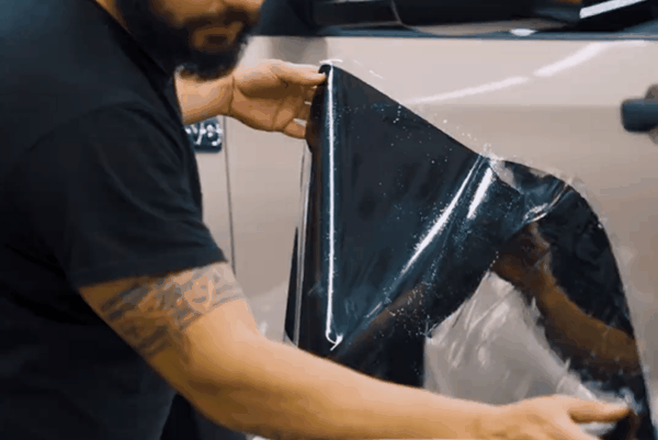 Technician installing dark automotive window tint film on a vehicle window.