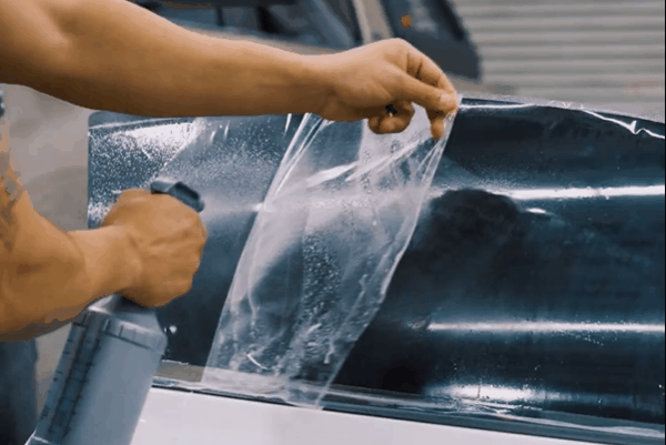 Technician spraying and positioning automotive window tint film on a vehicle window.