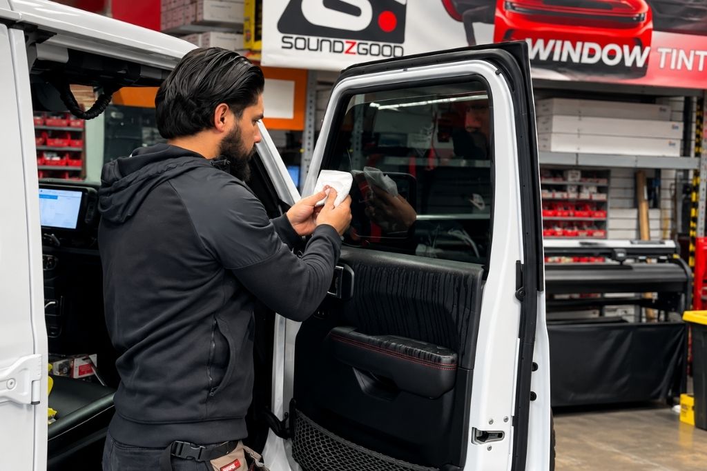 Technician installing window tint on a white vehicle at Soundz Good Garage automotive shop in Oxnard, CA.